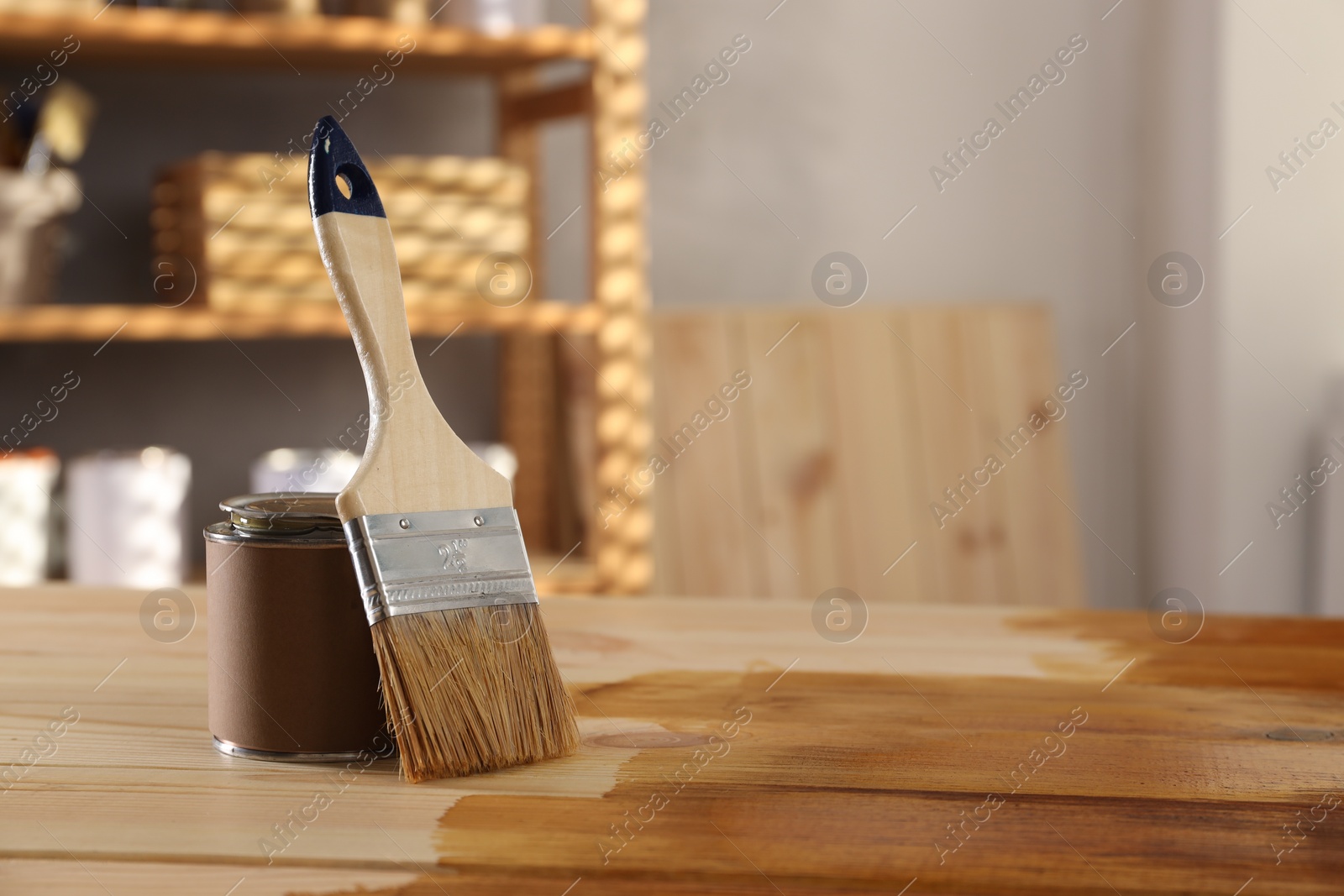 Photo of Brush and can with wood stain on wooden surface indoors, space for text