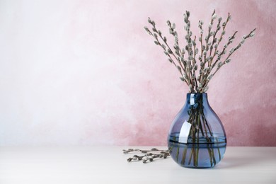 Photo of Beautiful bouquet of pussy willow branches in vase on white wooden table. Space for text