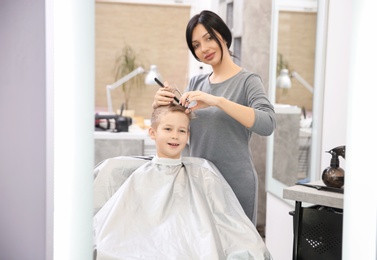 Photo of Professional female hairdresser working with little boy in salon