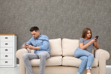 Photo of Couple engaged in smartphones while spending time together at home. Loneliness concept