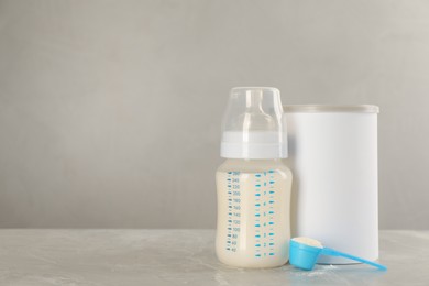 Photo of Blank can of powdered infant formula with feeding bottle and scoop on grey table, space for text. Baby milk