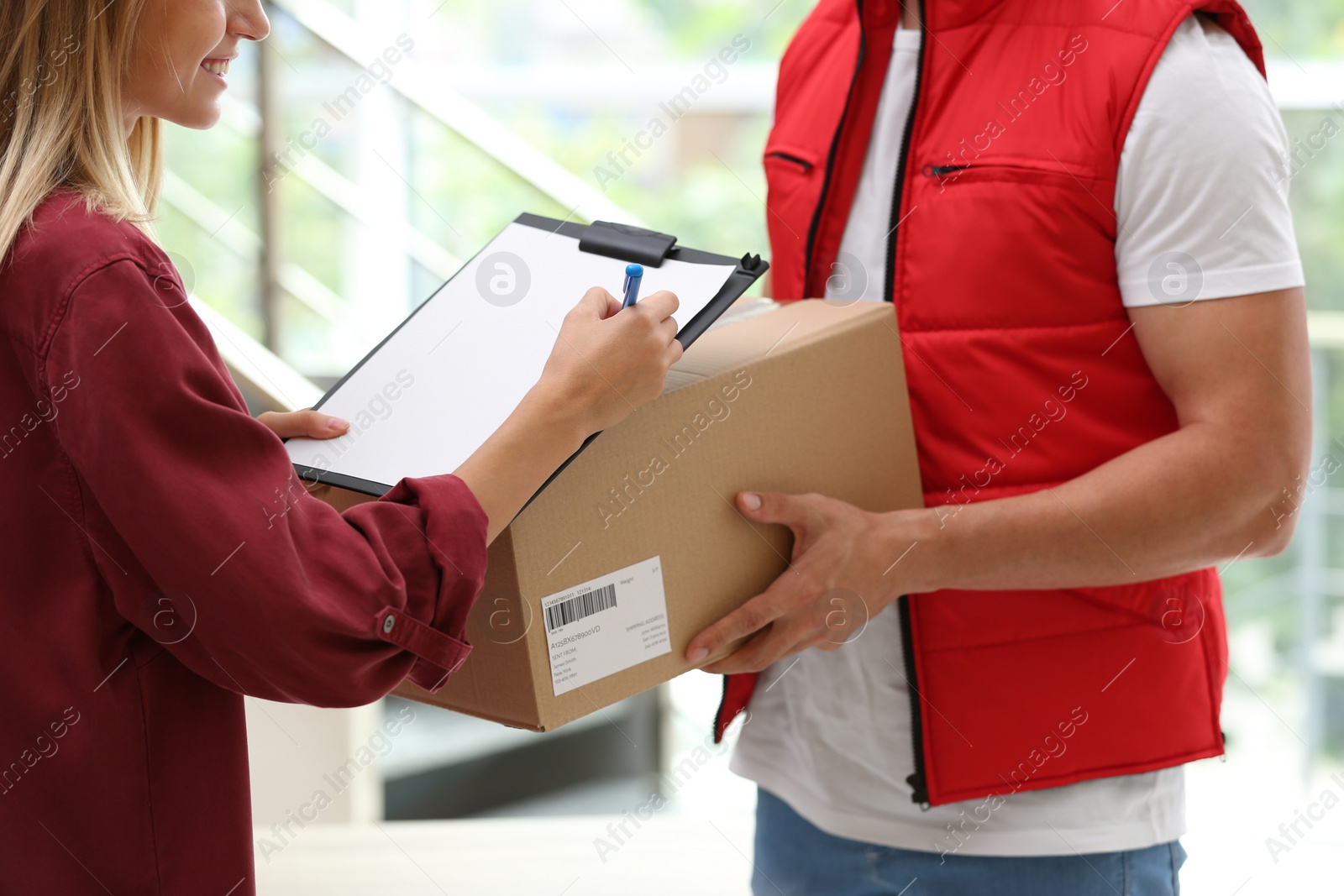 Photo of Young woman signing papers for delivered parcel indoors. Courier service