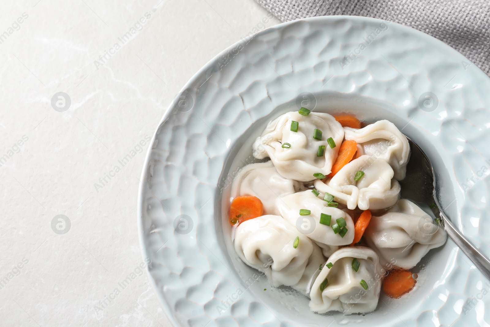 Photo of Plate of tasty dumplings in broth with spoon on grey marble table, top view. Space for text