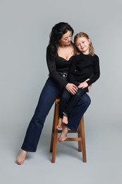 Photo of Beautiful mother with little daughter on stool against grey background
