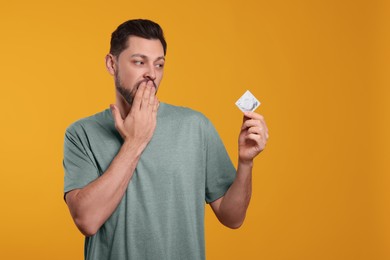 Photo of Confused man holding condom on orange background. Space for text
