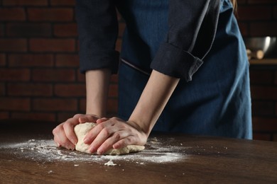 Photo of Making bread. Woman kneading dough at wooden table in kitchen, closeup