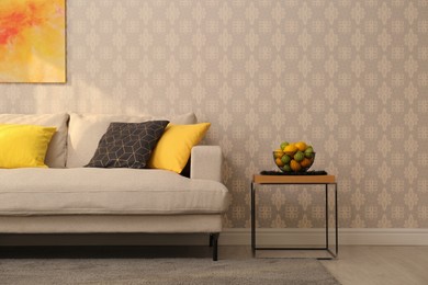 Image of Comfortable beige sofa and side table near wall. Minimalist living room interior