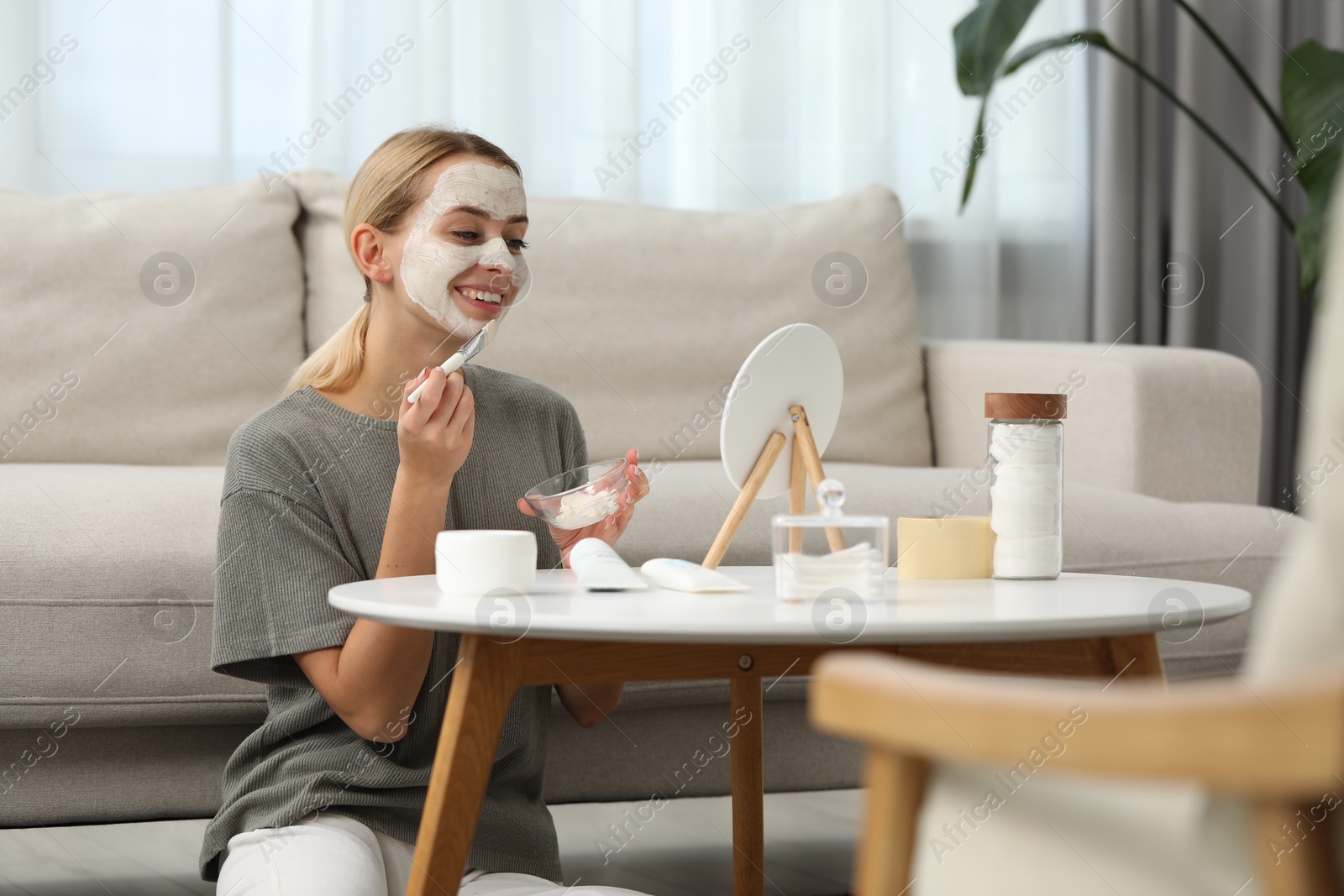 Photo of Young woman applying face mask in front of mirror at home. Spa treatments