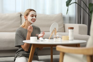 Photo of Young woman applying face mask in front of mirror at home. Spa treatments