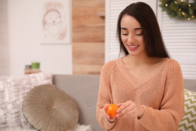 Photo of Happy young woman eating ripe tangerine at home
