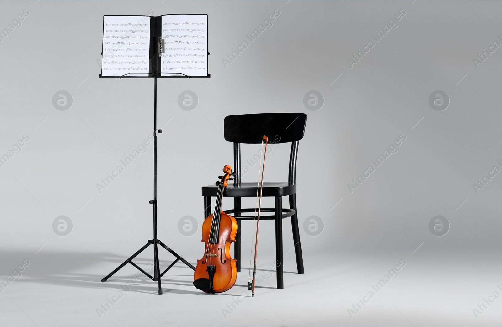 Photo of Violin, chair and note stand with music sheets on grey background. Space for text
