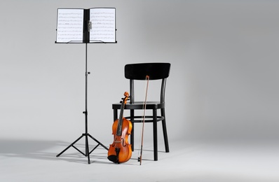 Violin, chair and note stand with music sheets on grey background. Space for text