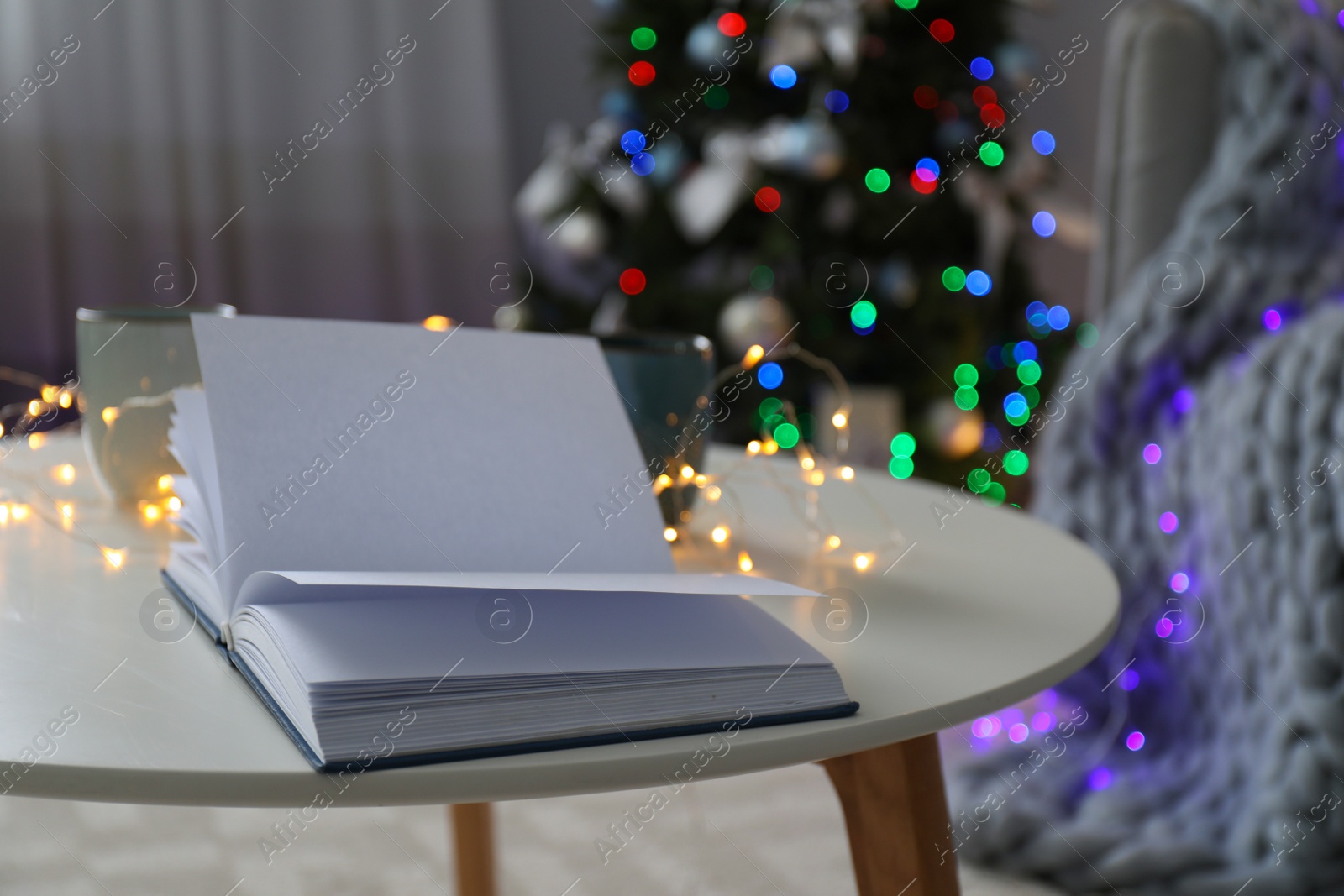 Photo of Open empty book on table and Christmas tree in room