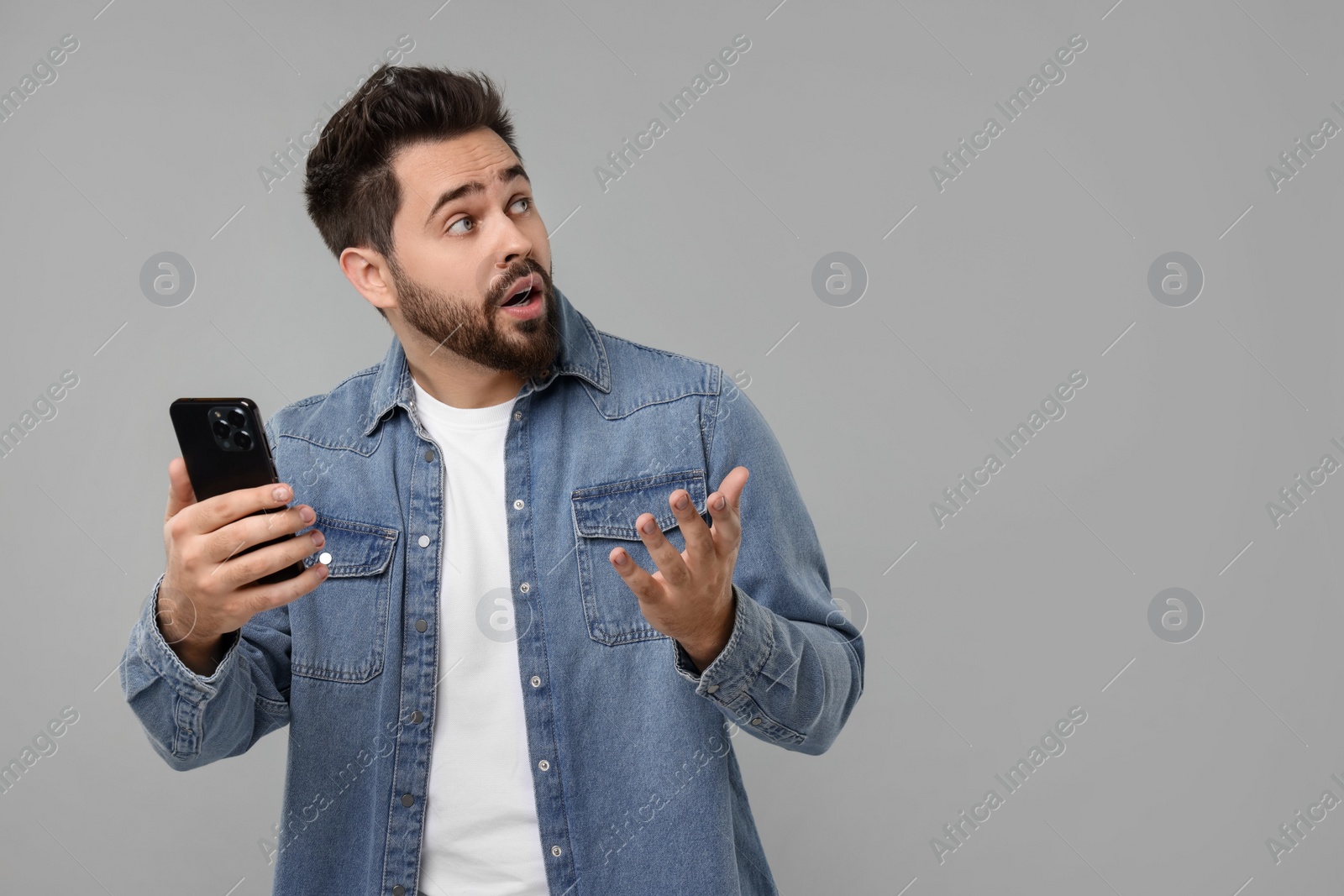 Photo of Emotional man using smartphone on grey background, space for text