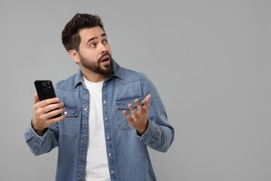 Emotional man using smartphone on grey background, space for text