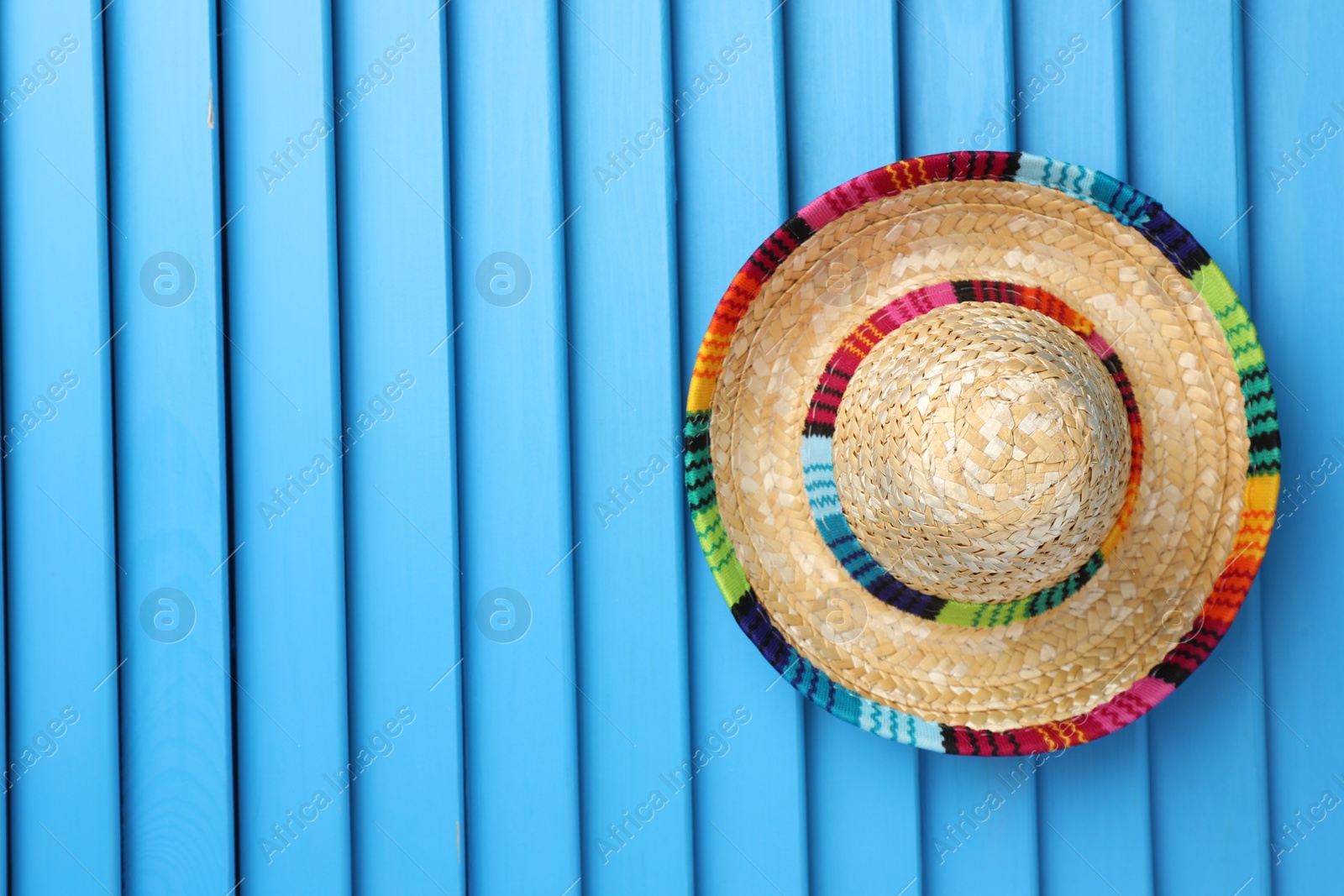 Photo of Mexican sombrero hat on blue wooden surface, top view. Space for text