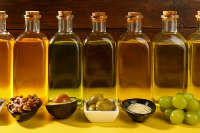 Photo of Vegetable fats. Different oils in glass bottles and ingredients on yellow table, closeup