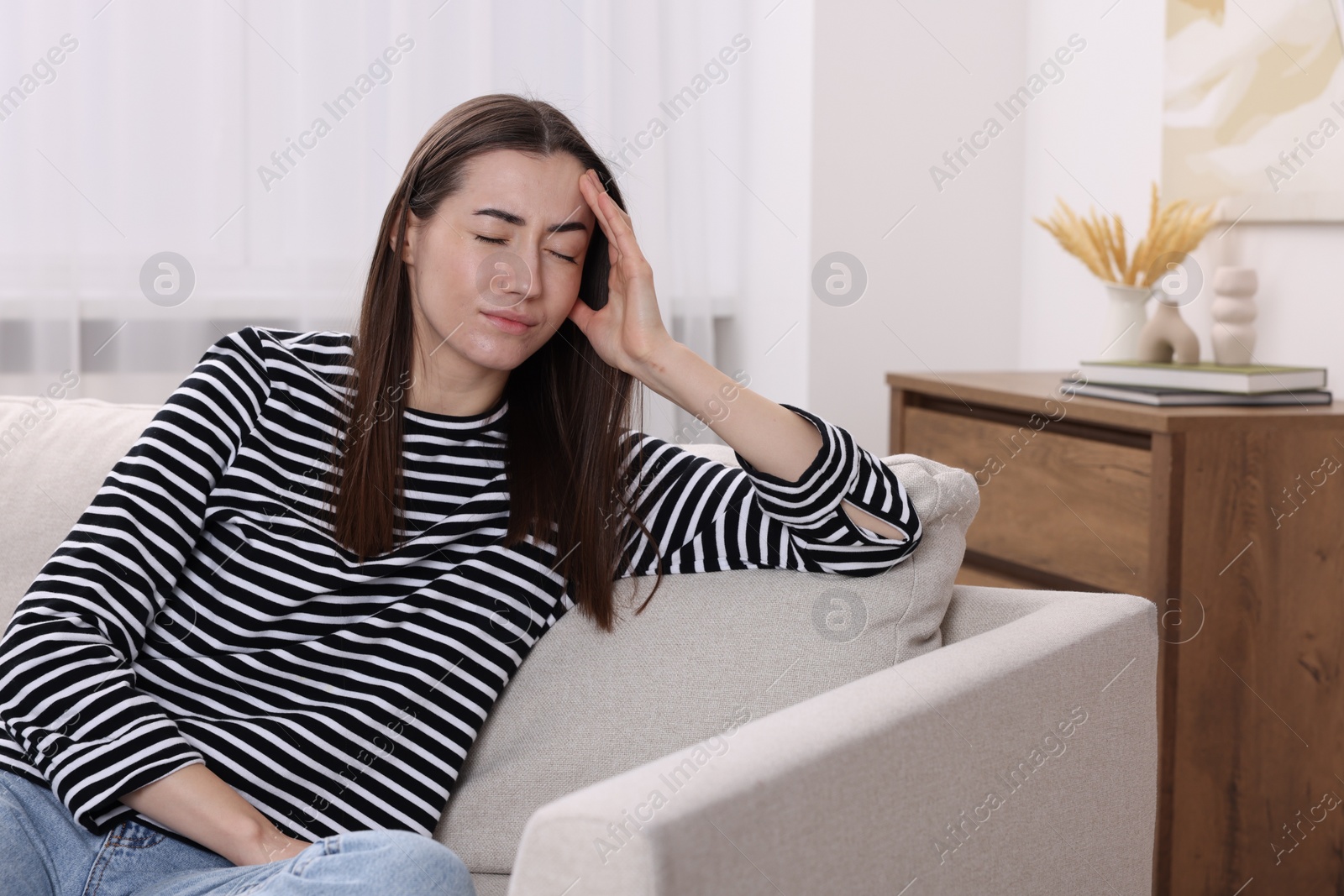 Photo of Sad woman suffering from headache on sofa indoors