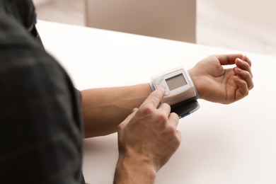 Photo of Man checking blood pressure with sphygmomanometer at table, closeup. Cardiology concept