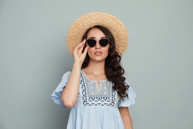 Photo of Beautiful young woman with straw hat and stylish sunglasses on light grey background