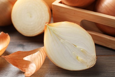 Whole and cut onions on wooden table, closeup