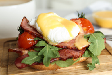 Photo of Delicious egg Benedict served on wooden board, closeup