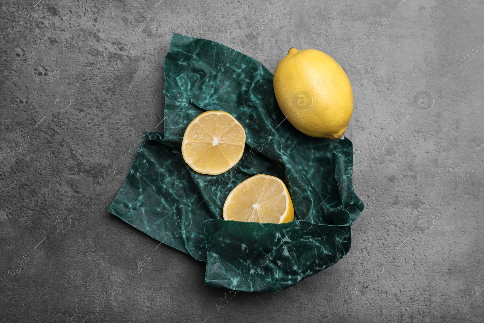 Photo of Whole and cut fresh lemons with beeswax food wrap on grey table, flat lay