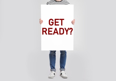 Image of Man holding poster with text Get Ready? on light grey background, closeup