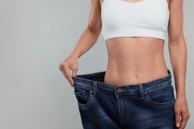 Slim woman wearing big jeans on grey background, closeup and space for text. Weight loss