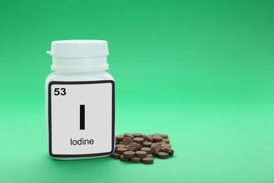 Photo of Plastic jar and iodine pills on green background. Space for text