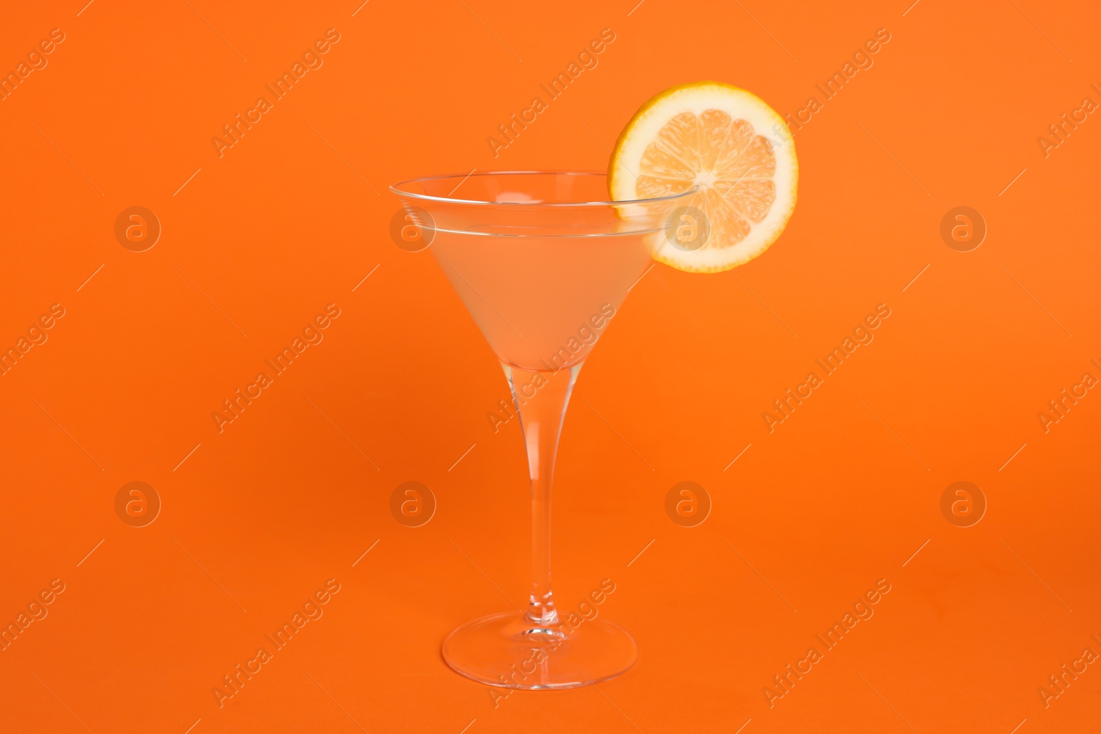 Photo of Martini glass of refreshing cocktail with lemon slice on orange background