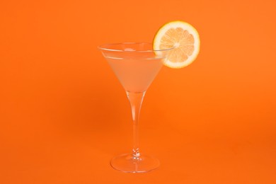 Photo of Martini glass of refreshing cocktail with lemon slice on orange background