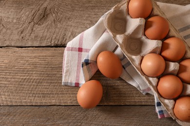 Raw chicken eggs in carton and napkin on wooden table, flat lay. Space for text