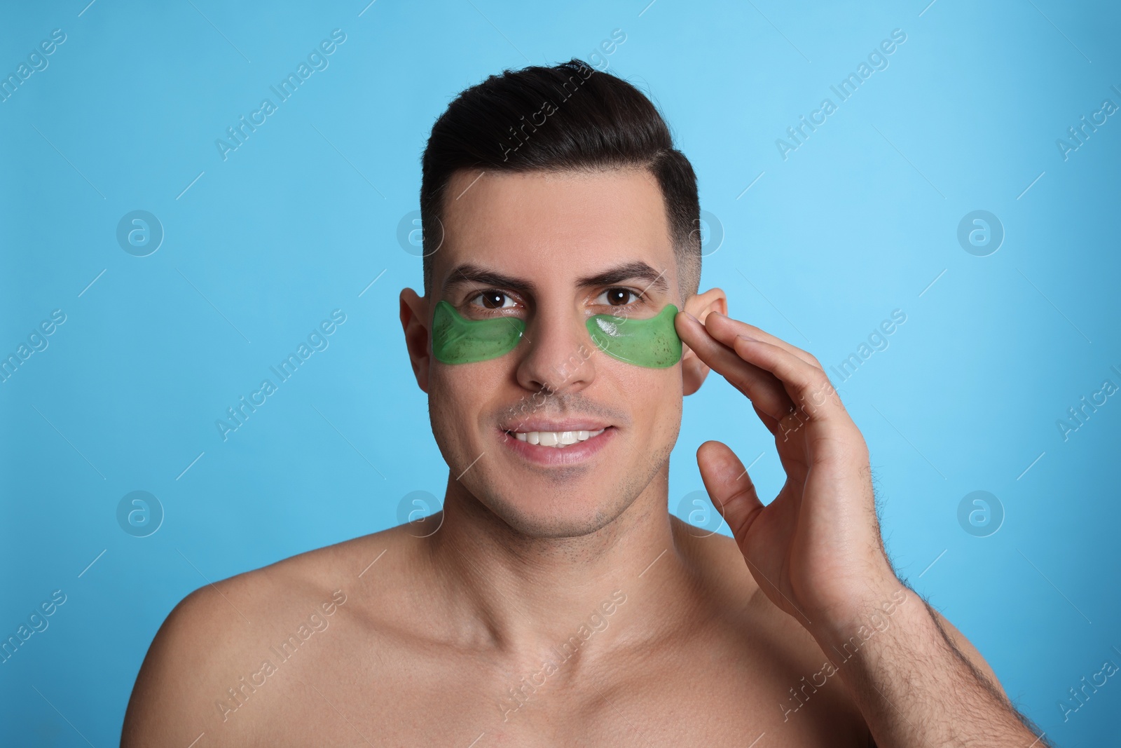 Photo of Man applying green under eye patch on light blue background