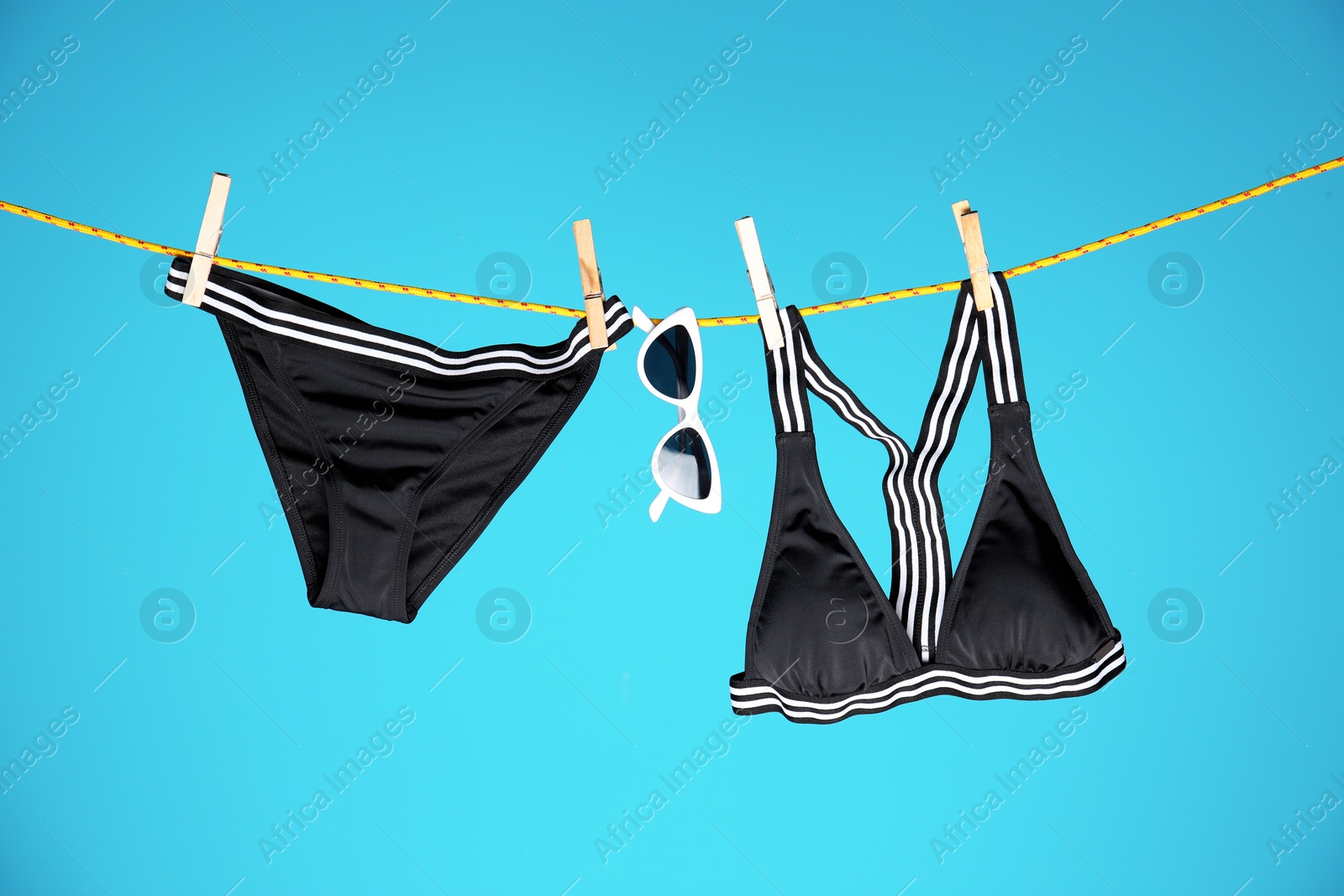 Photo of Beautiful bikini and sunglasses hanging on rope against color background