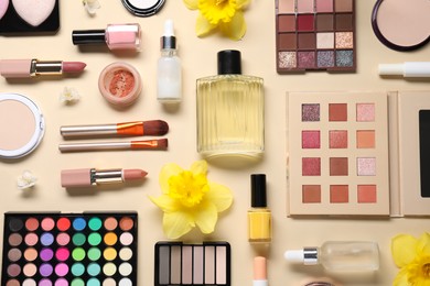 Photo of Flat lay composition with different makeup products and beautiful spring flowers on beige background