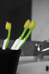 Light green toothbrushes in black toothbrush holder indoors