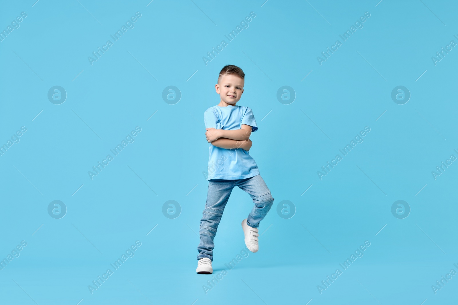 Photo of Happy little boy dancing on light blue background