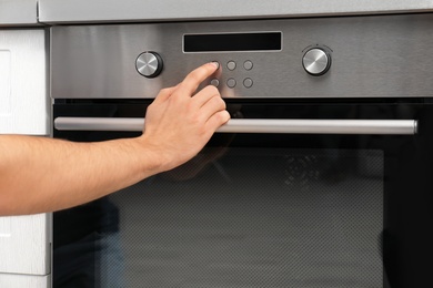 Young man adjusting oven settings in kitchen, closeup