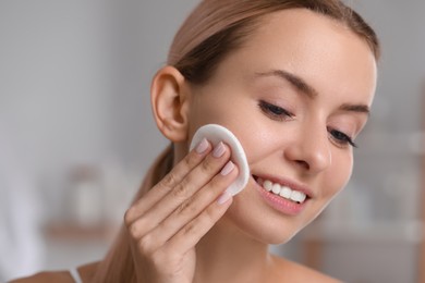 Smiling woman removing makeup with cotton pad indoors, closeup