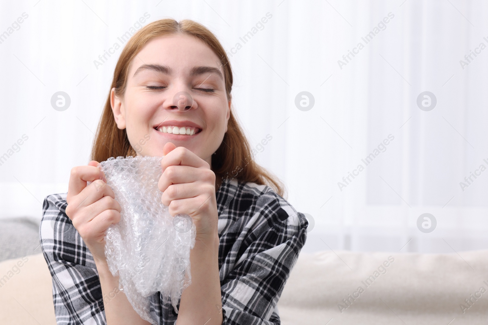 Photo of Woman popping bubble wrap on sofa at home, space for text. Stress relief