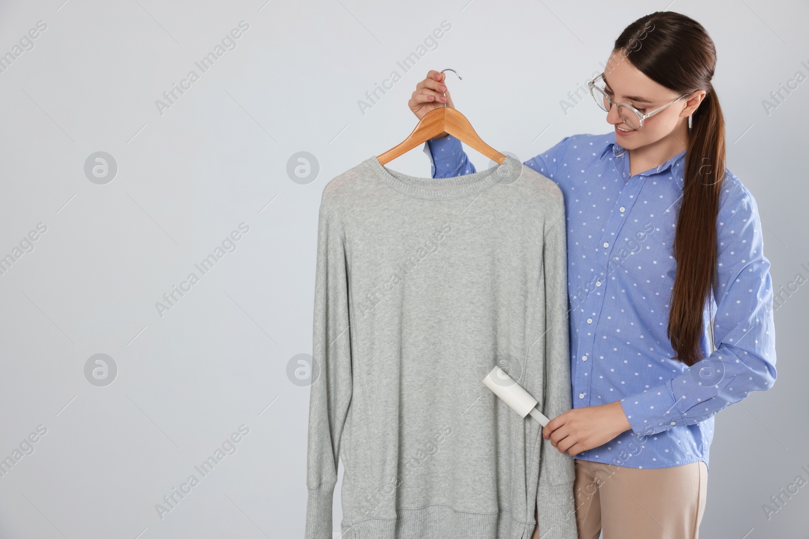 Photo of Woman cleaning clothes with lint roller on light grey background, space for text