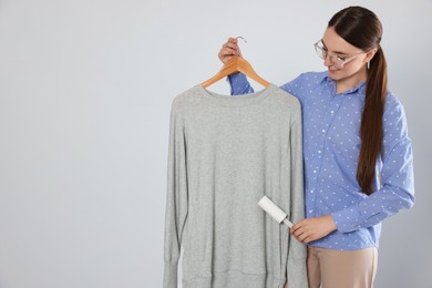 Photo of Woman cleaning clothes with lint roller on light grey background, space for text