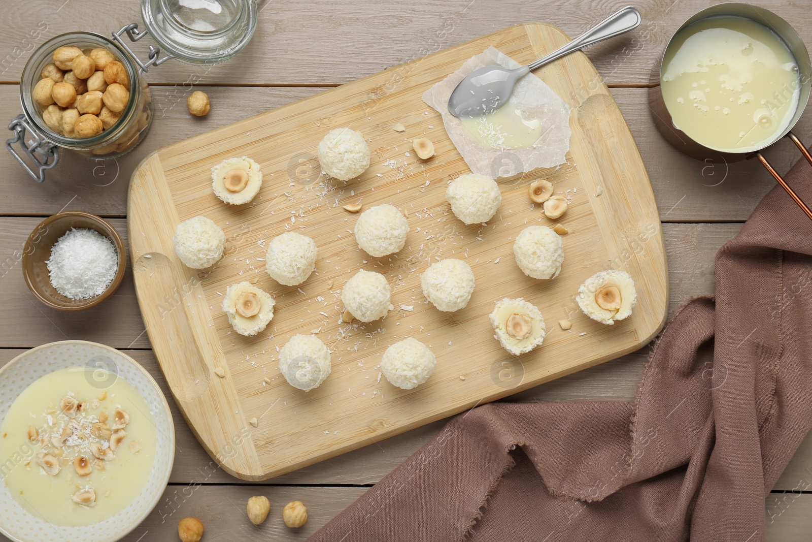 Photo of Delicious candies with coconut flakes, hazelnut and ingredients on wooden table, flat lay