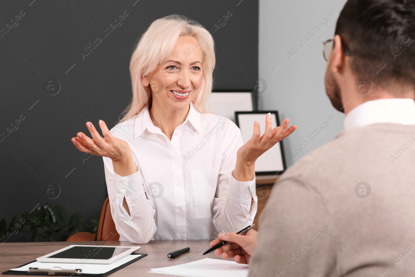 Photo of Happy woman having conversation with man at wooden table in office. Manager conducting job interview with applicant