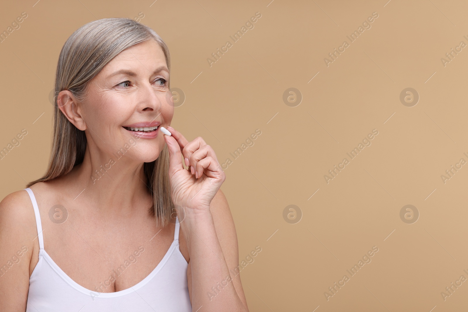 Photo of Beautiful woman taking vitamin capsule on beige background, space for text