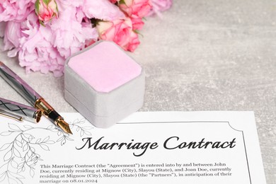 Photo of Marriage contract, fountain pen, jewelry box and flowers on grey table, closeup