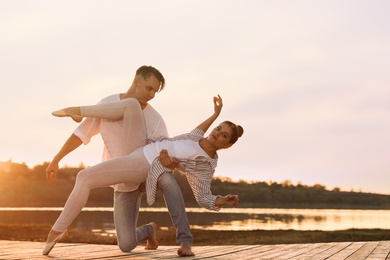 Photo of Beautiful young couple practicing dance moves near river at sunset