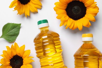 Photo of Bottles of cooking oil and sunflowers on white table, flat lay