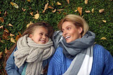 Photo of Portrait of happy mother and her daughter on green grass with autumn leaves outdoors, top view